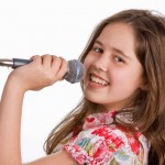 Pretty young girl smiling whilst holding a microphone and singing
